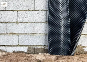 Kurz vor dem Noppenbahn-Verlegen, lehnt die Rolle an einer grauen Mauer.